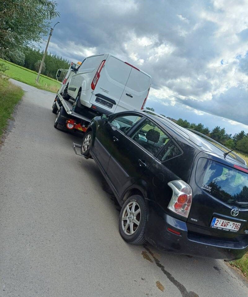 Takelwagen met een bestelwagen op de laadbak en een tweede wagen op sleep langs een landelijke weg