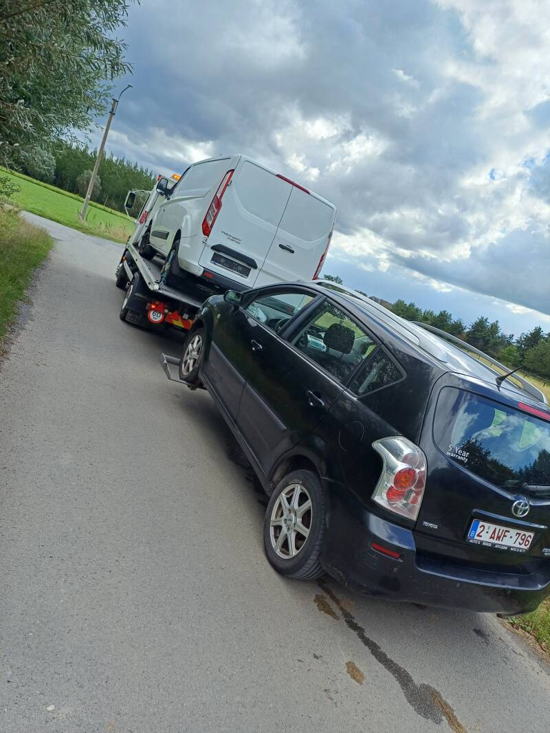 Takelwagen met een bestelwagen op de laadbak en een tweede wagen op sleep langs een landelijke weg