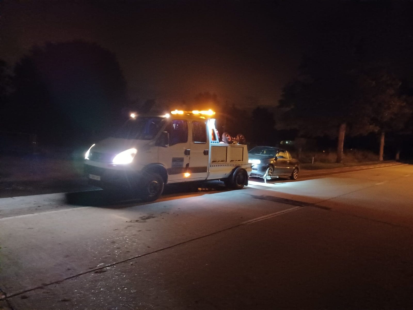 Takelwagen met zwaailichten aan tijdens een nachtelijke interventie langs de weg